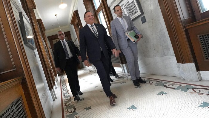 François Legault, accompagné de trois personnes, marche dans les couloirs de l'Assemblée nationale. 