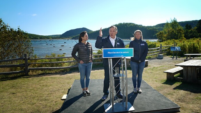 François Legault se trouve devant le parc national du Bic, accompagné de la candidate pour Rimouski, Maïté Blanchette-Vézina, ainsi que d'Isabelle Charest, ancienne ministre des Sports.