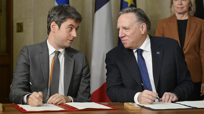 Deux hommes politiques signent des documents en se regardant.
