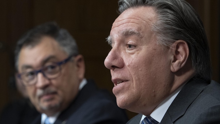 Le premier ministre parle tandis que, un peu derrière lui, le Dr Horacio Arruda le regarde et l'écoute.