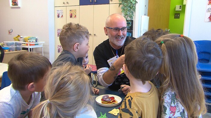 François Marceau est entouré d'enfants, il leur montre des jouets. 
