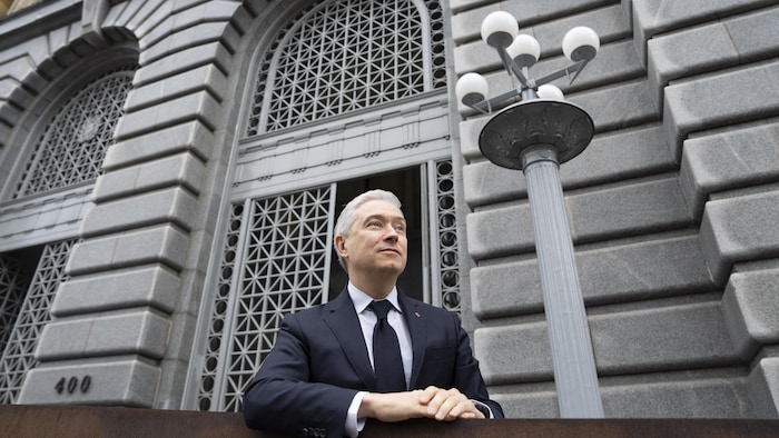 Il est devant un bâtiment en béton.