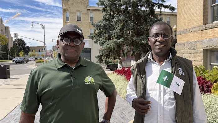 Deux hommes posent à l’extérieur de l’hôtel de ville de St. Thomas, vêtus de vert et de blanc.