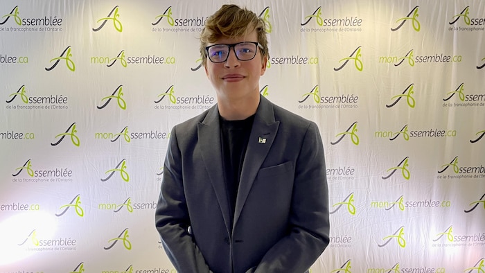 Un jeune souriant avec des lunettes regarde droit devant.