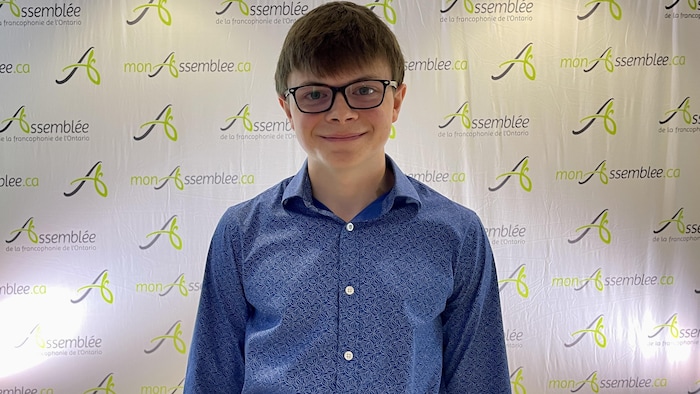 Une jeune souriant avec des lunettes regarde droit devant.