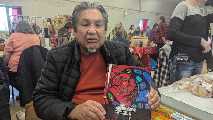 Frank Polson tient dans ses mains son livre à son kiosque dans un marché de Noël.