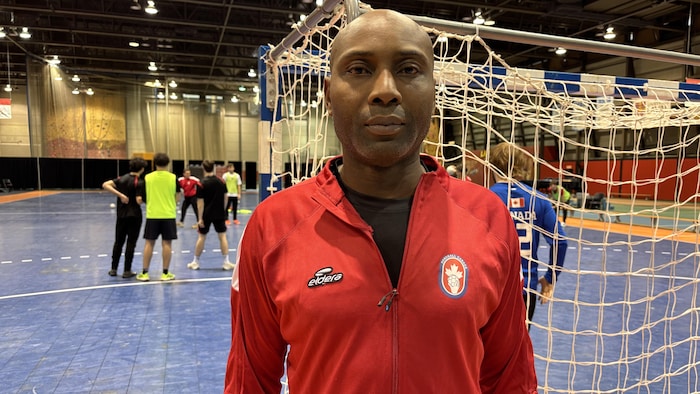 Il pose pour la photo devant un filet de handball.