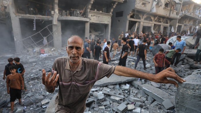 Un homme fait un geste tandis que des Palestiniens inspectent le site d’une frappe israélienne contre une maison.