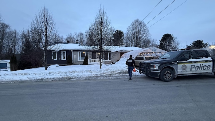 Un véhicule de la Sûreté du Québec devant une maison et un policier.