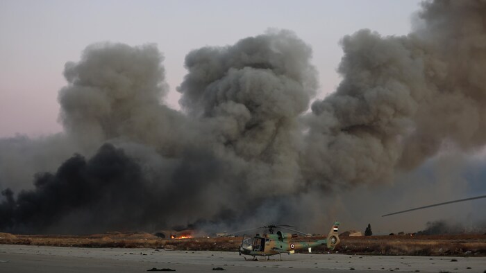 Smoke rises near a helicopter.