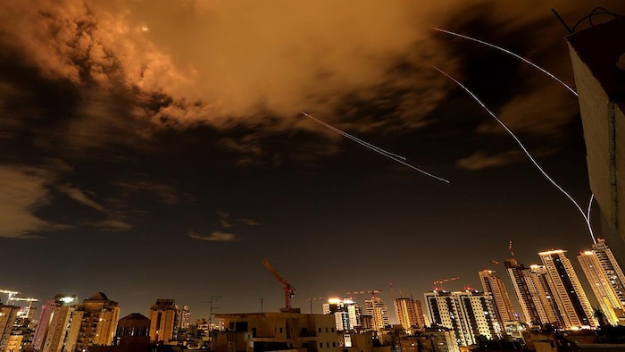 Des traînées lumineuses et de la fumée sont visibles dans le ciel israélien au-dessus d'une ville.
