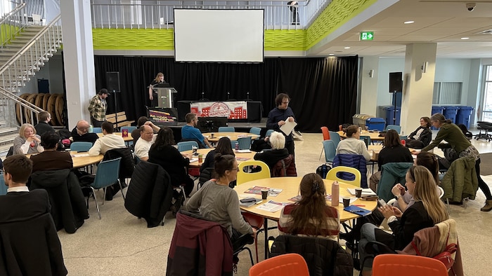 Des gens sont assis à des tables devant une personne qui fait une présentation.