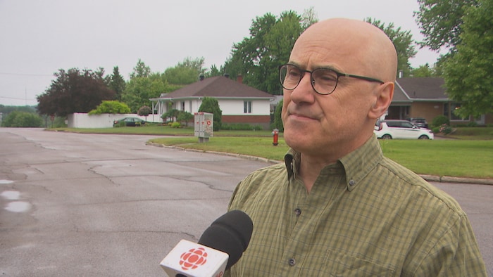 Un homme parle au micro de Radio-Canada dans la cour de sa maison. 