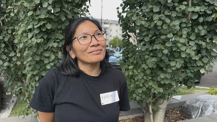 Ferch Reynoso, portant des lunettes et un chandail noir, se tient à l’extérieur devant des arbres. Une étiquette portant son prénom est fixée sur son chandail.