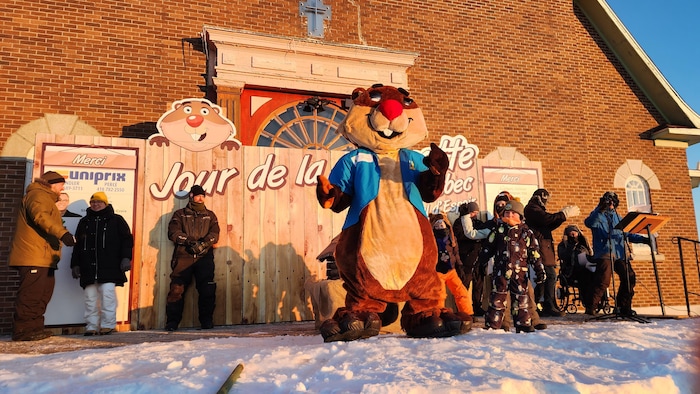 Une mascotte de la marmotte et des gens qui s'amusent dans le froid derrière.