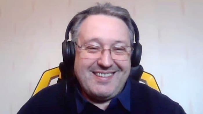 Frédéric Aitken, portant un casque d'écoute, apparaît par webcam et sourit.