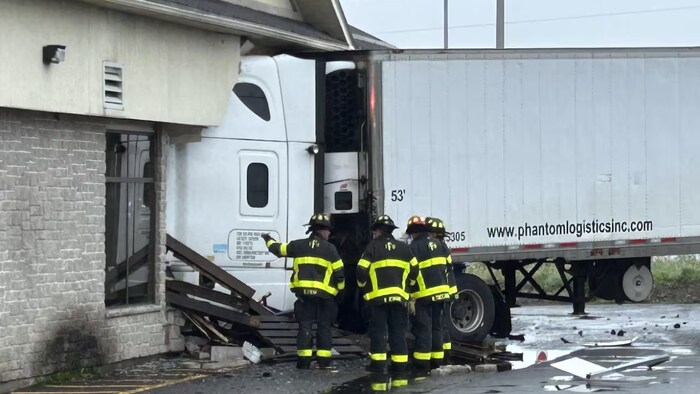 Trois pompiers examinent la cabine du camion qui se trouve dans le bâtiment.