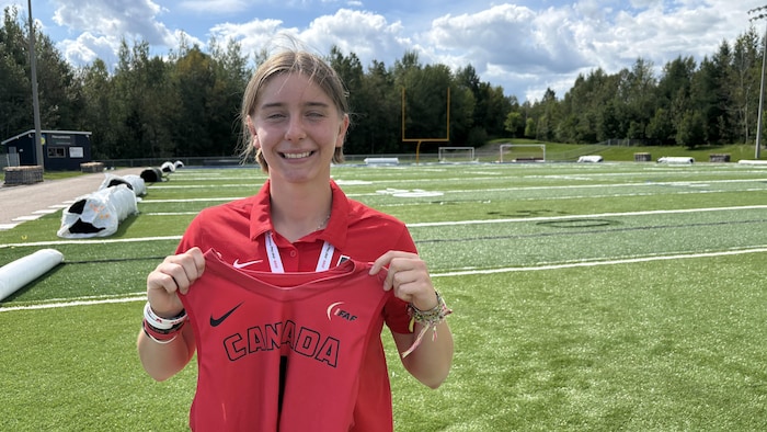 Elle posent sur un terrain de football, son gilet de l'équipe canadienne en main devant elle.