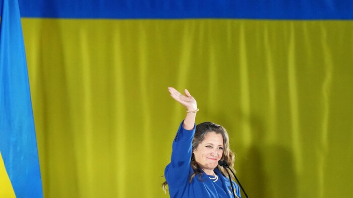 Chrystia Freeland salue la foule devant un drapeau ukrainien.