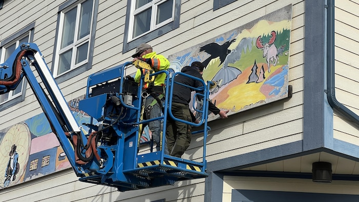 Des personnes dans une échelle mécanique retirent une fresque d'un bâtiment.