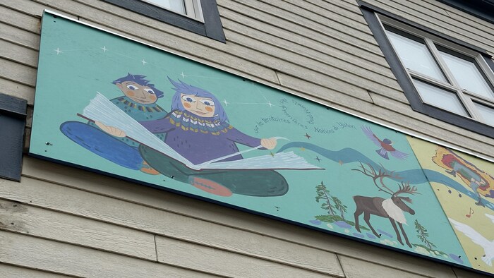 Le premier panneau d'une fresque montre deux enfants en train de lire un grand livre duquel une rivière jaillit.
