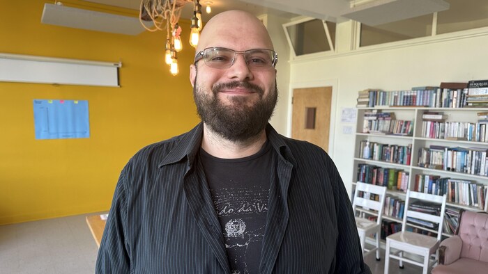 Un homme se tient dans un local avec une bibliothèque derrière lui.