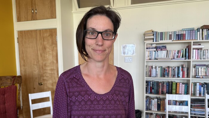 Une femme se tient dans un local devant une bibliothèque.