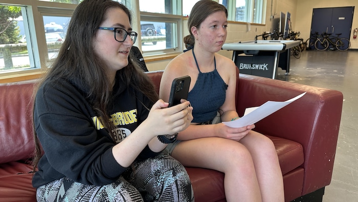 Deux élèves sur un sofa, avec un téléphone et des questions sur papier en main.