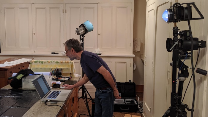 Michel Élie devant un ordinateur portable dans une pièce avec un lumière à rayonnement ultraviolet.