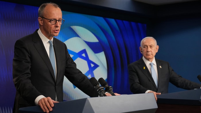 Devant un écran qui projette l'image du drapeau d'Israël, Friedrich Merz parle derrière un lutrin pendant que Benyamin Nétanyahou, à ses côtés, écoute lors d'une conférence de presse.