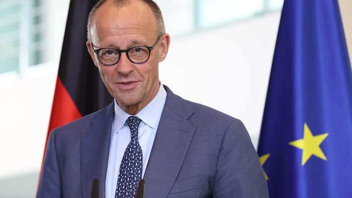 Friedrich Merz devant des drapeaux de l'Allemagne et de l'Union européenne.
