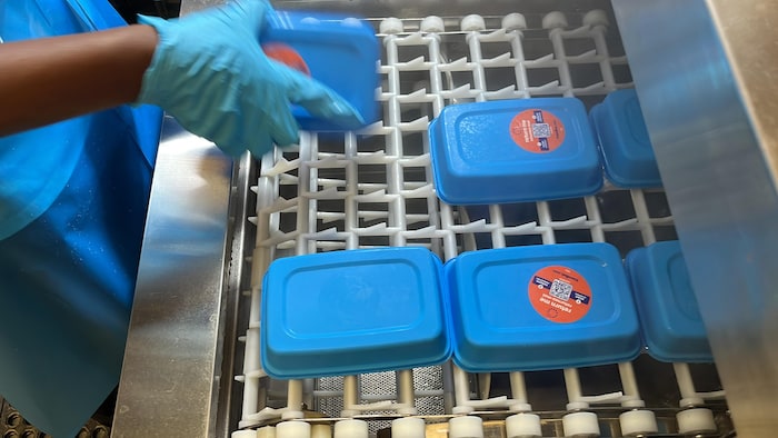 Une employée prépare des contenants afin qu'ils soient nettoyés dans un lave-vaisselle.
