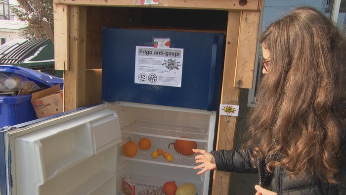 Une femme montre un réfrigérateur.