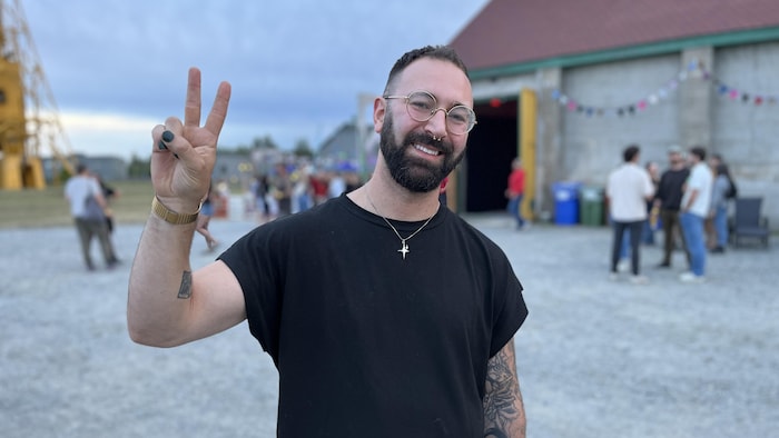 Charles-Antoine Chouinard pose sur le site de la Cité de l'Or, souriant, faisant un signe de paix avec ses doigts.