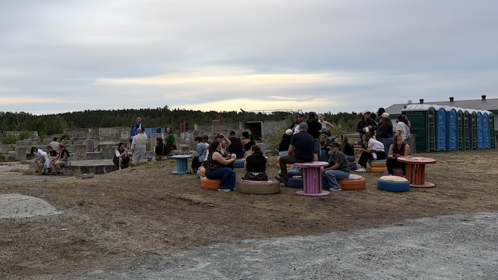 Des gens sont assis sur des pneus ou des tabourets colorés sur le site extérieur de la Cité de l'Or.