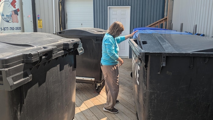 La présidente de l'organisme s'apprête à regarder le contenu d'énormes poubelles à l'extérieur.