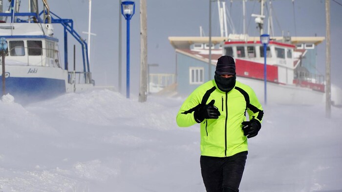 Un homme court en tenue d'hiver dans le blizzard, près de bateaux.