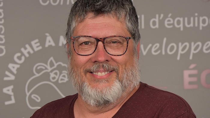 Jacquelin Sévigny pose en souriant devant un mur illustré avec le logo de La Vache à Maillotte.