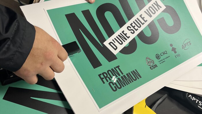 Une personne broche sur un carton une affiche sur laquelle il est écrit « Front commun ».