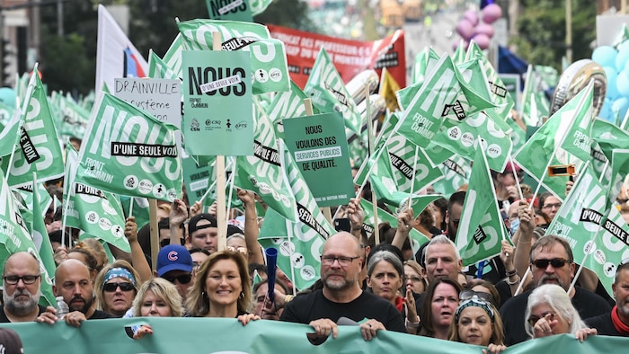 Derrière une banderole verte, des milliers de manifestants brandissent des drapeaux verts.