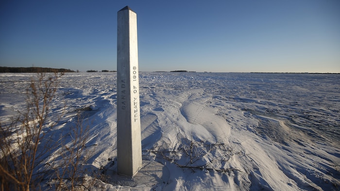 Un marqueur à la frontière entre le Canada et les États-Unis au Manitoba, dans un champ couvert de neige.