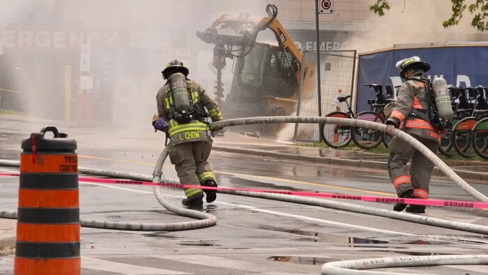 Deux pompiers traînent un boyau sur un chantier de construction.
