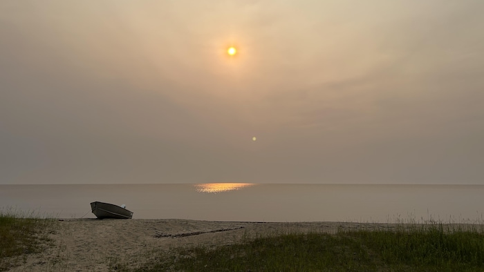 Une chaloupe sur une plage du Lac-Saint-Jean avec le soleil voilé dans le ciel.