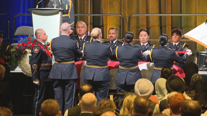 Des agents correctionnels en uniforme plient le drapeau canadien au-dessus d'un cercueil.