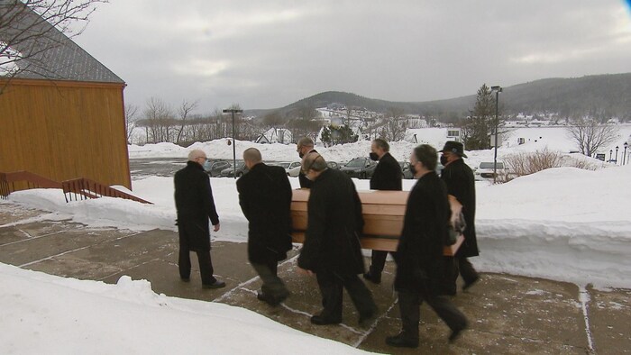 Six hommes portent le cercueil de Jules Bélanger.