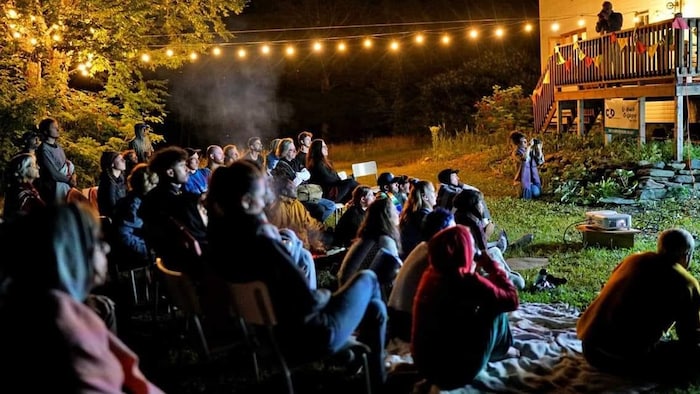 Des dizaines de personnes sont assises sur l'herbe dans la cour arrière du Salon58 pour assister à une projection d'un film de danse.