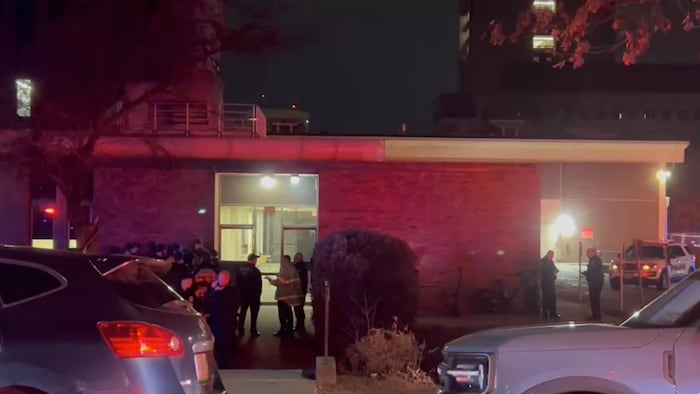 Un groupe de policiers sont rassemblés à l'extérieur d'un édifice et attendent pour intervenir.