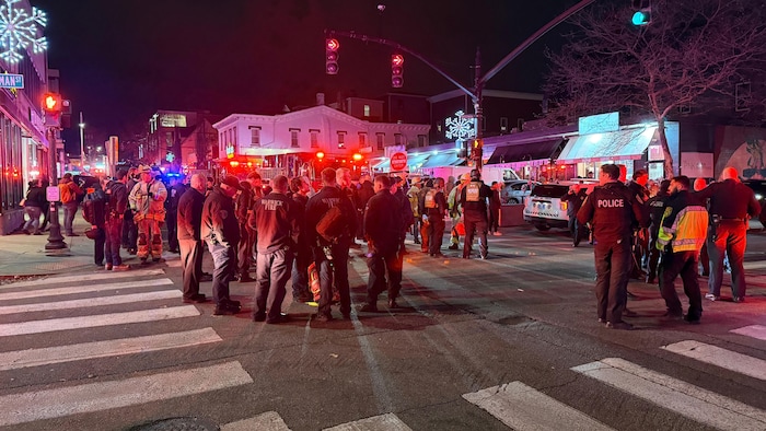 Un attroupement de personnes dont des pompiers et des policiers au coin d'une rue.