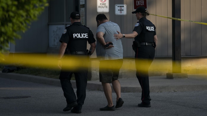Des policiers réconfortent un homme sur les lieux d’une fusillade qui a fait trois morts dans le secteur de North York, à Toronto.