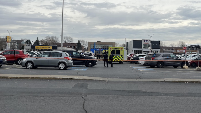 Des policiers dans un stationnement près d'un cordon de sécurité.